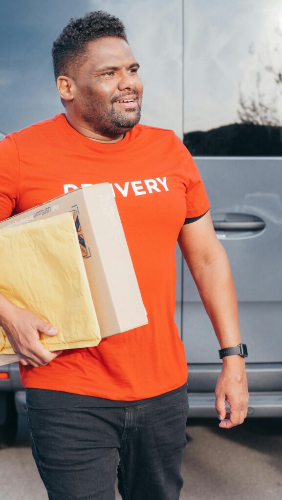 African American courier in a red shirt delivers packages with a smile outdoors. Perfect for delivery service concepts.